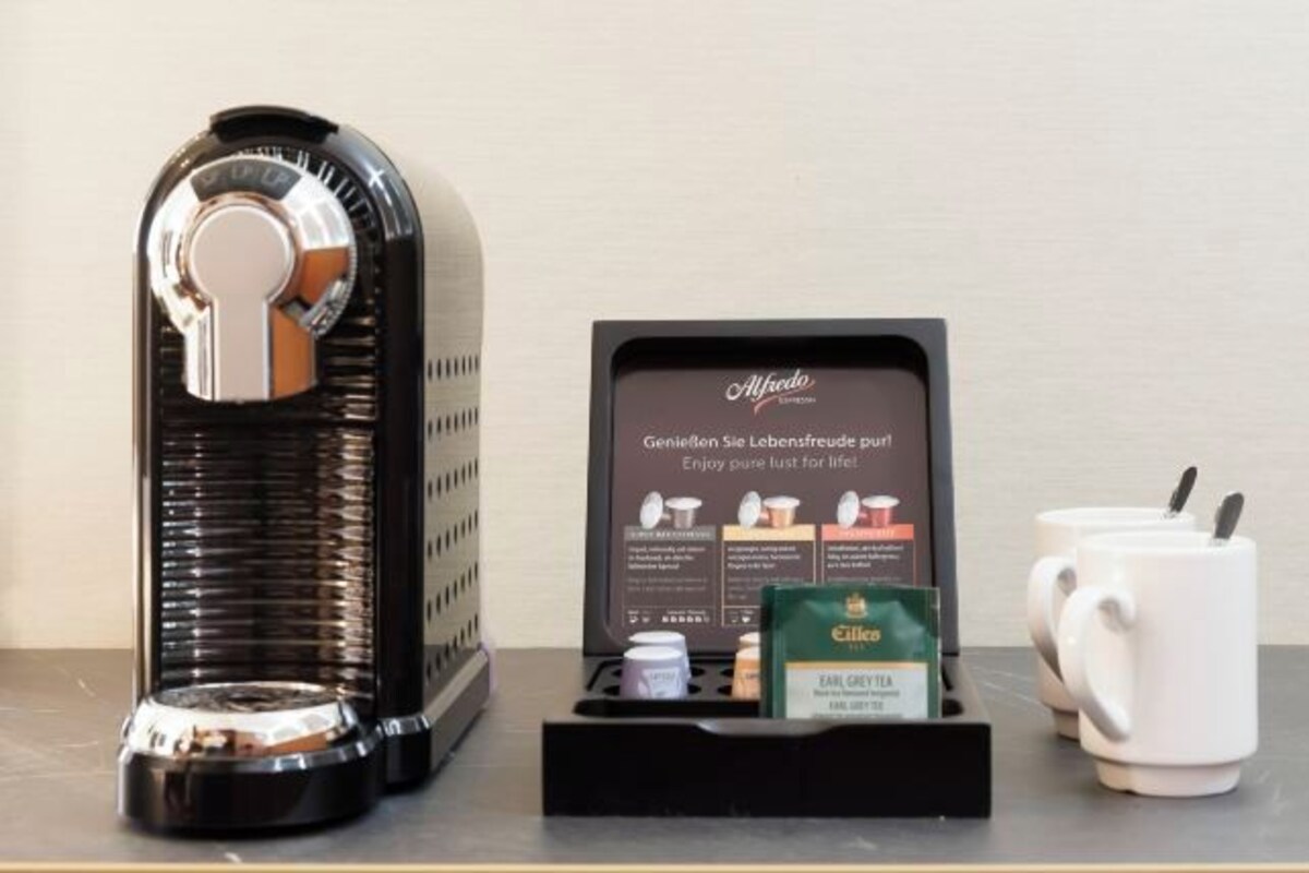 En kaffemaskin, ett ställ med kaffekapslar och två vita muggar på ett bord.