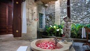 Una bañera de piedra llena de pétalos de rosa, una pared de piedra con una ventana y una estatua de un mono sosteniendo una flor.