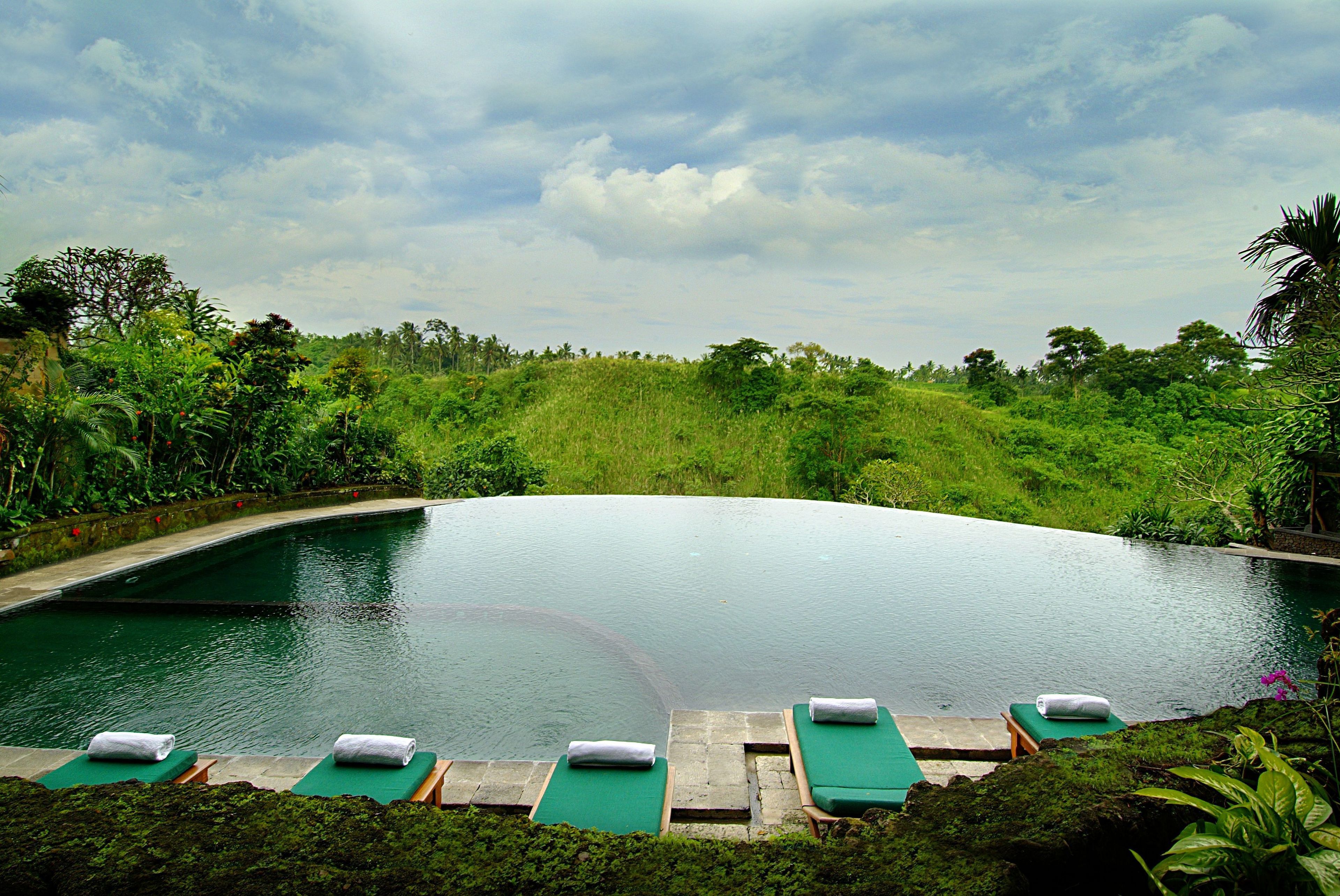 A serene outdoor swimming pool with lounge chairs and a lush green landscape in the background.