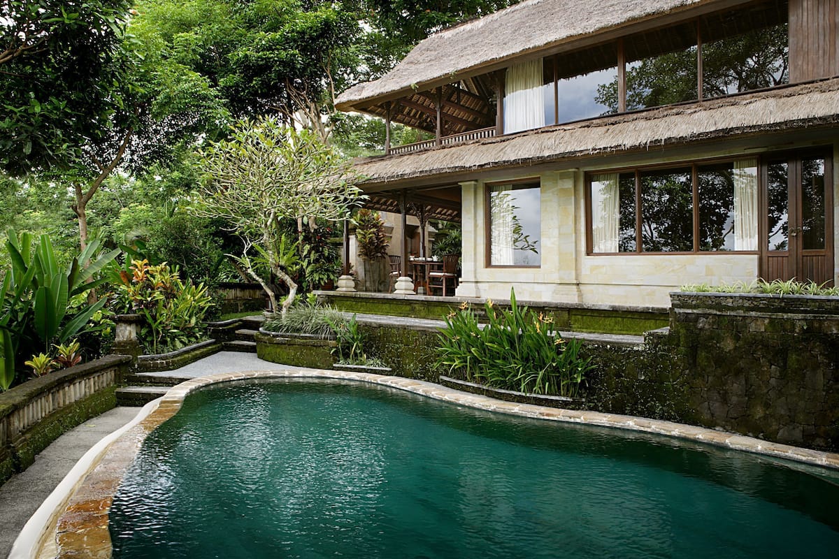 A pool surrounded by lush greenery and a house with a thatched roof.