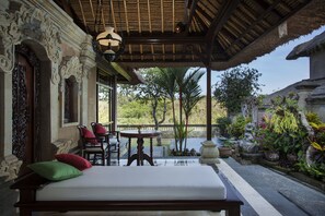 A room with a bed, a table, and chairs, a view of a garden with a water feature, and a thatched roof. - Pita Maha (Ubud)