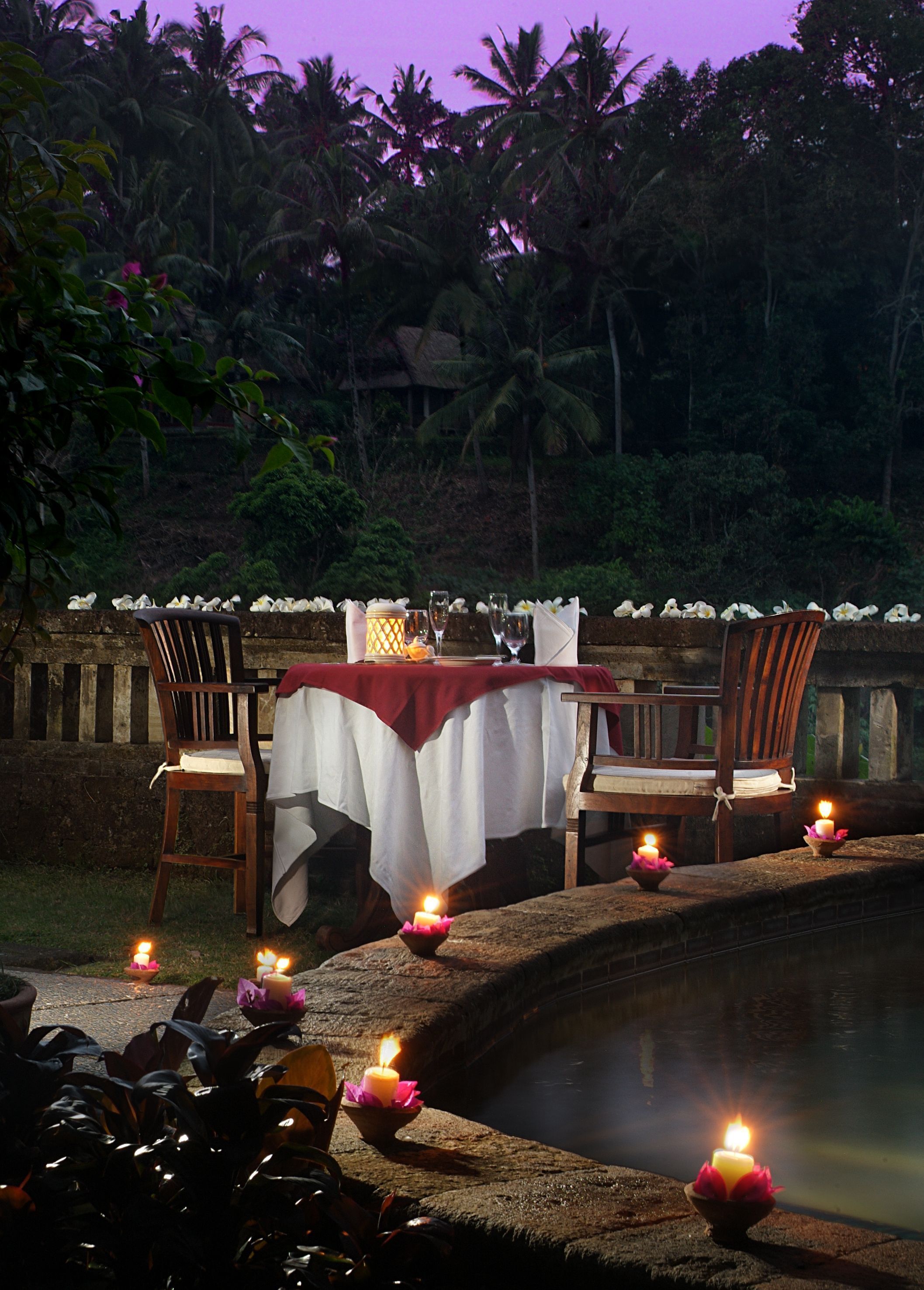 A dining table set for two with candles and flowers, overlooking a water feature.