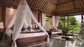Un dormitorio lujoso con cama a dosel, un rincón de descanso con sofá y vistas a exuberante vegetación.