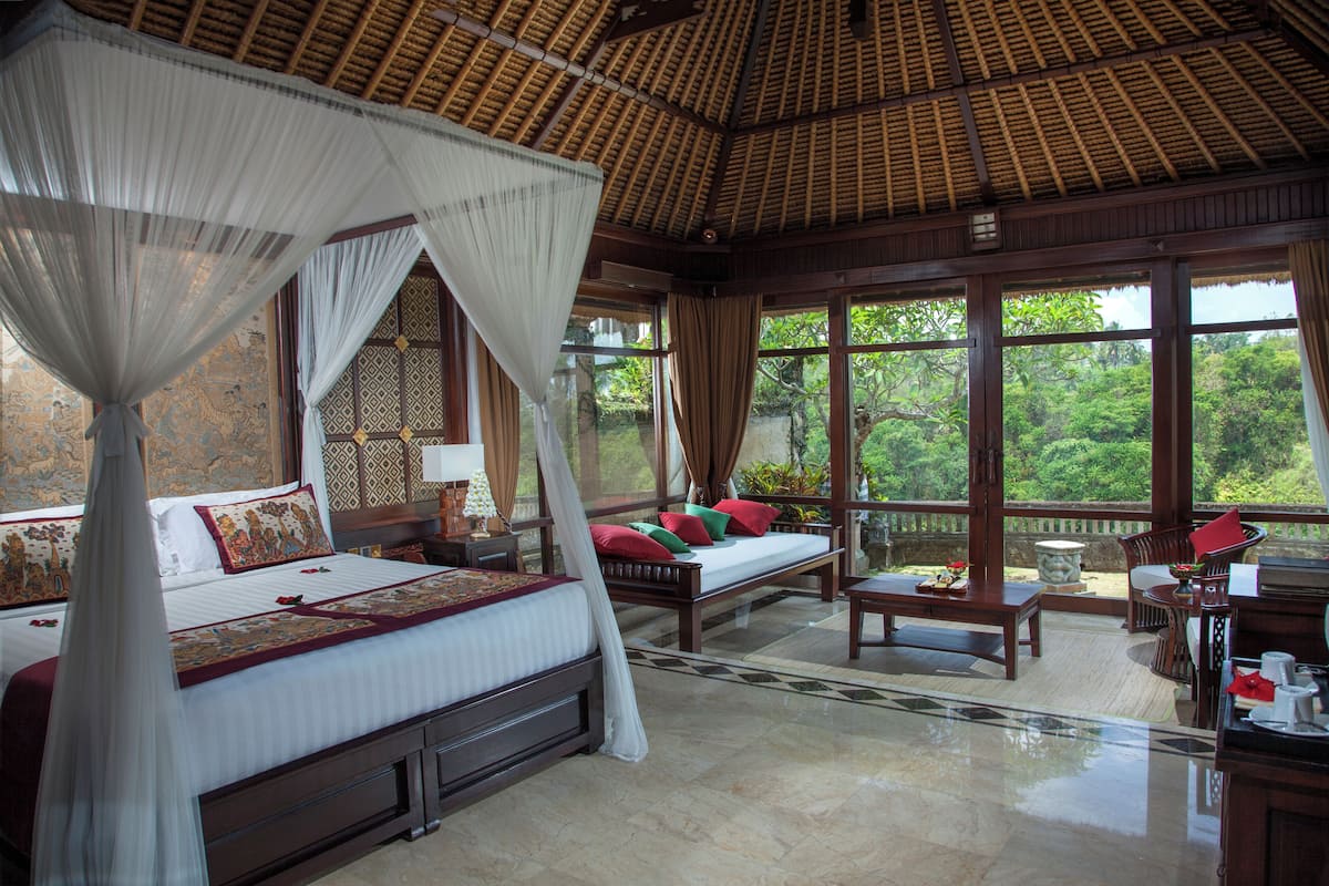A spacious bedroom with a large bed, a sitting area, and a balcony with a view of the greenery.