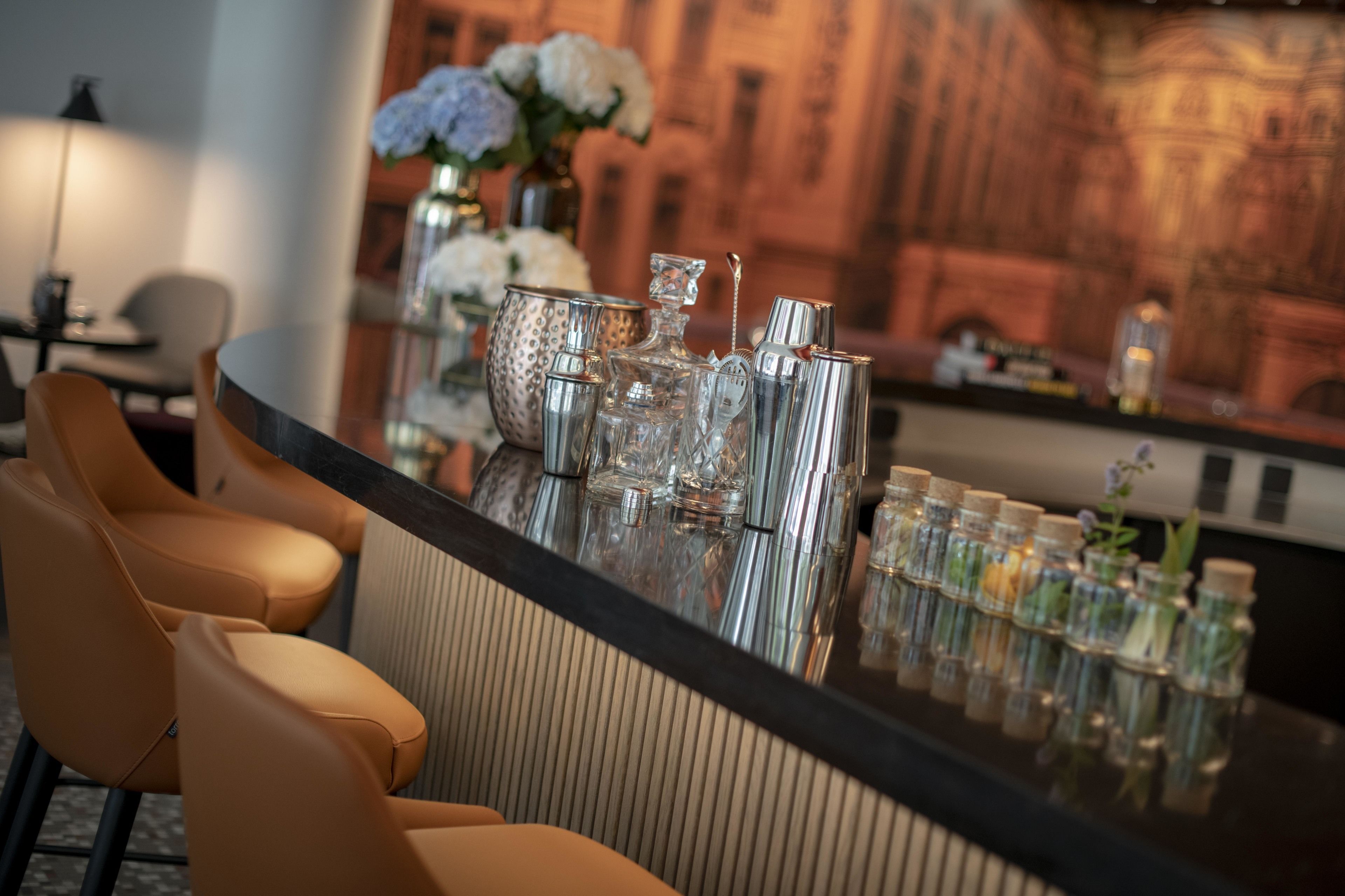 A bar area with a polished bar counter, a selection of bar tools, and a vase with flowers.