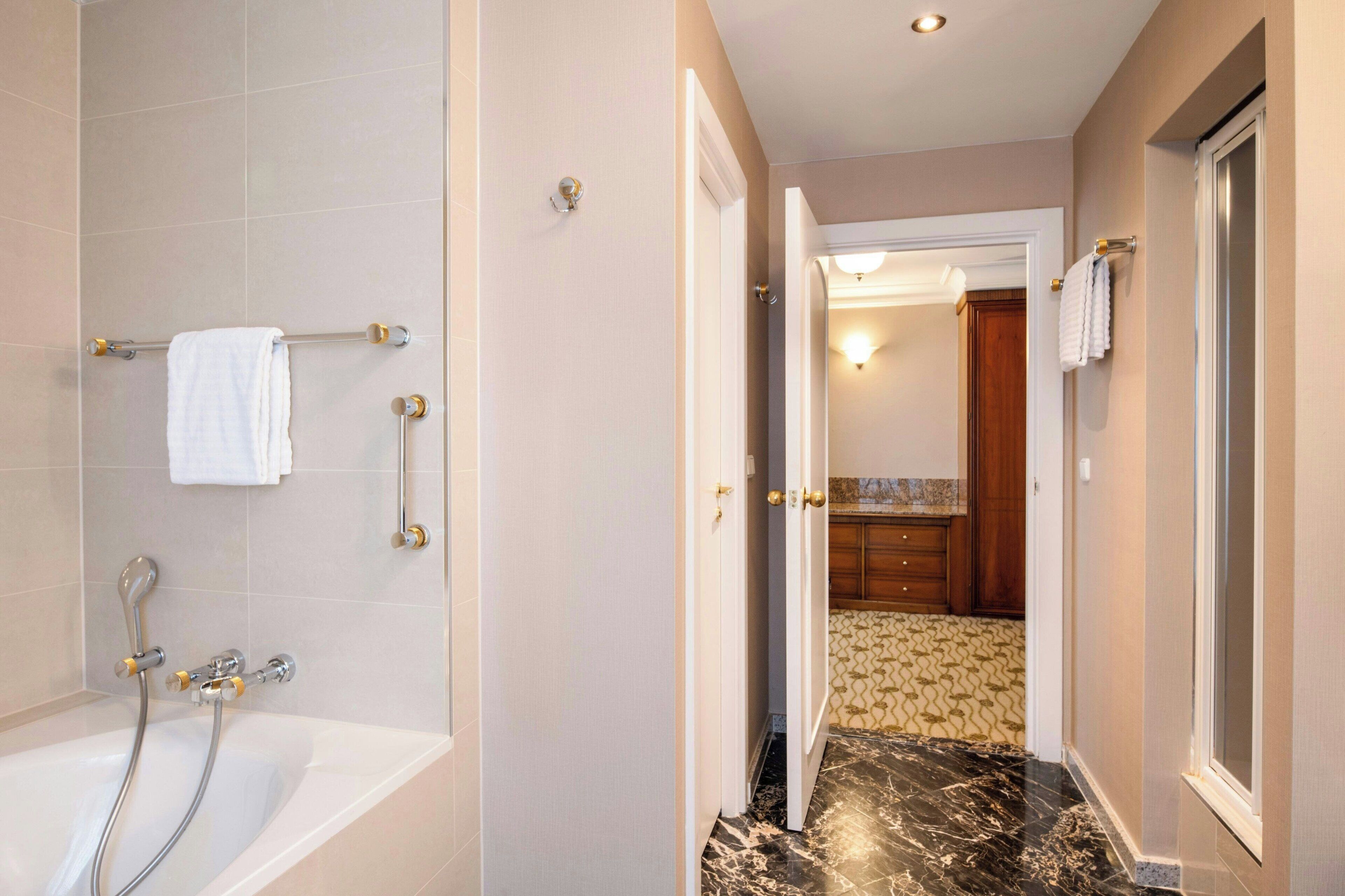 Baño con bañera, ducha y puerta visible que da a una zona de cocina.