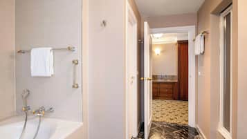 Baño con bañera, ducha y puerta visible que da a una zona de cocina.