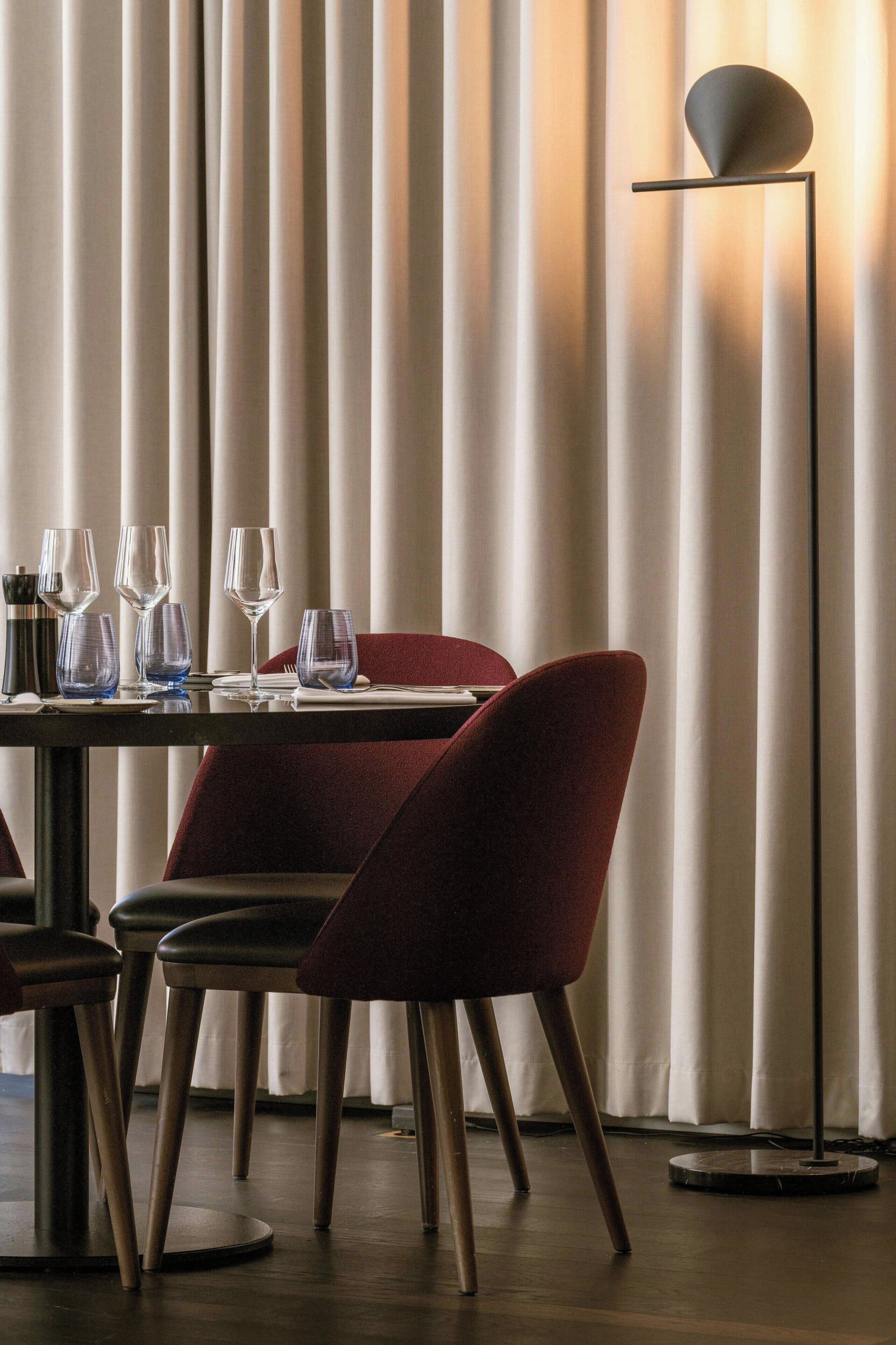 A dining area with a table set for two, chairs, and a floor lamp.