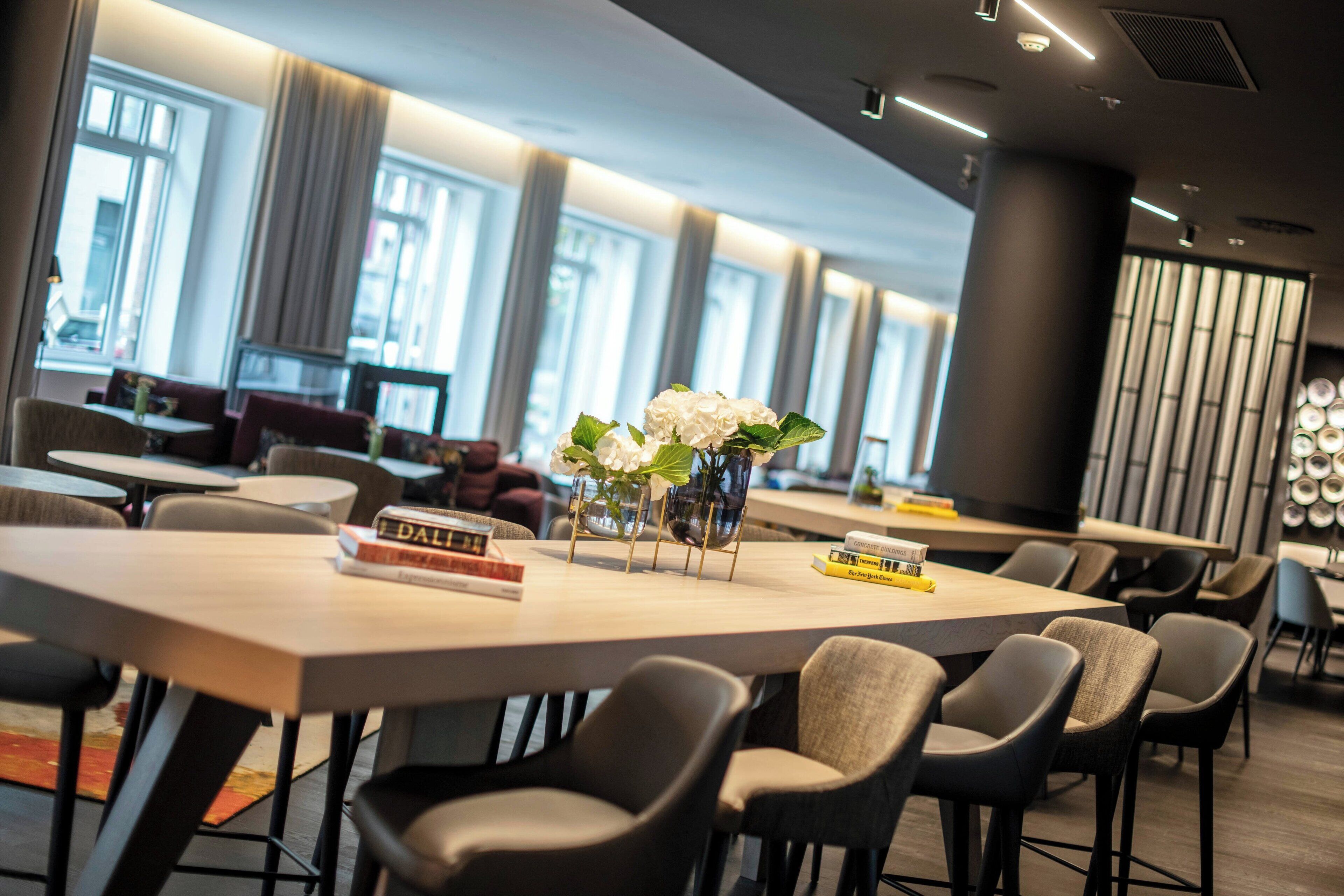 Een moderne eetruimte met ronde tafels en stoelen, een vaas met witte bloemen en boeken op de tafels.