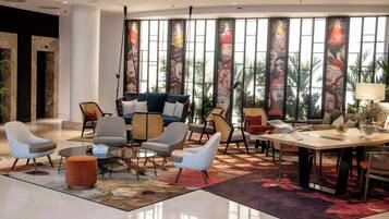 Een ruime woonkamer met modern meubilair, grote ramen met kunstwerken en uitzicht op palmbomen.