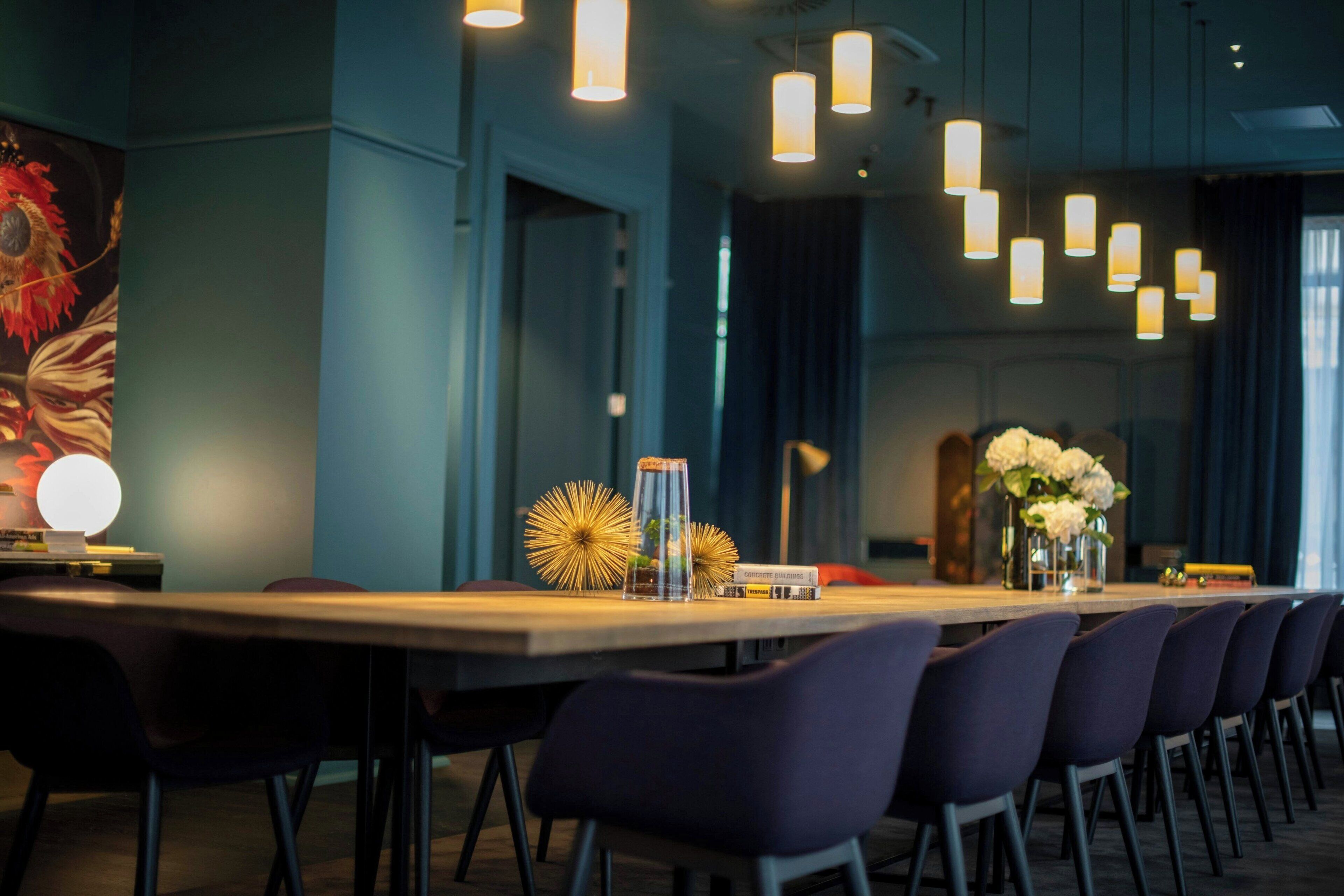 Une longue table entourée de chaises, avec des luminaires suspendus et des objets décoratifs.