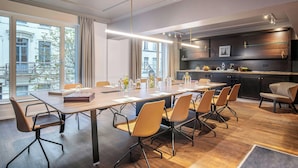 A modern conference room with a long table, multiple chairs, and a kitchen area with a dark wood finish and modern appliances.