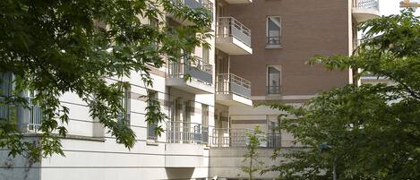A multi-story residential building with balconies, a paved courtyard, and surrounding greenery.