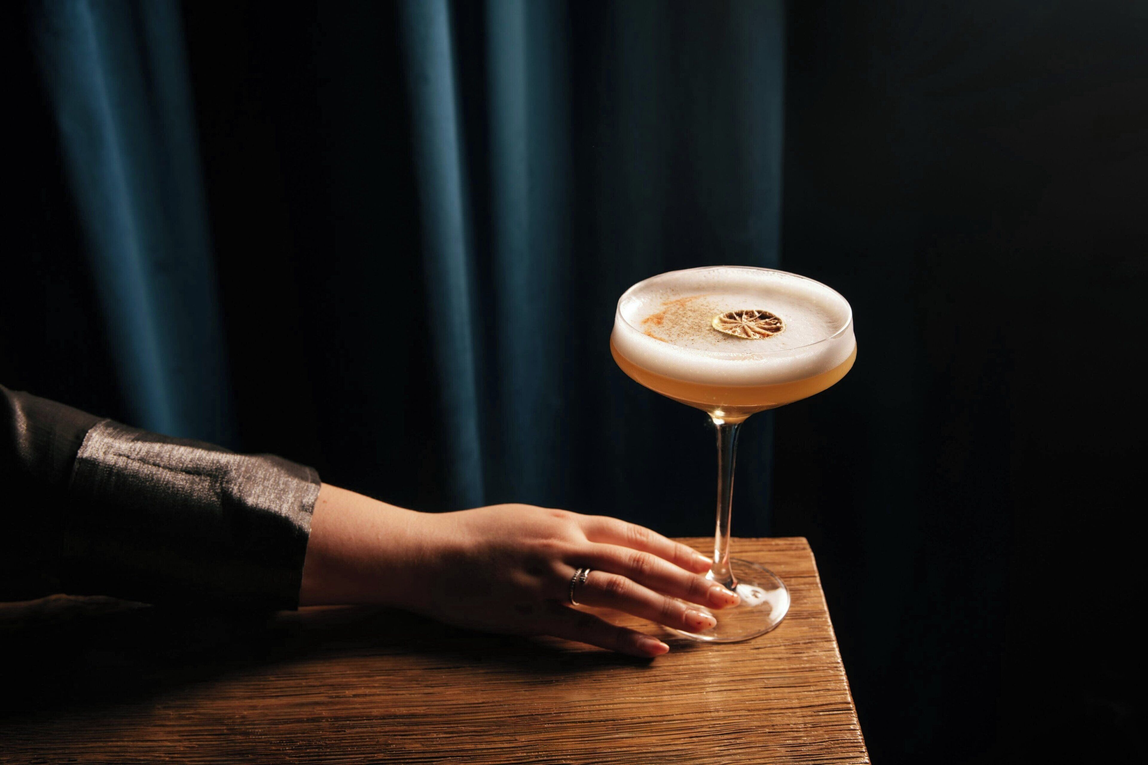 A hand holding a martini glass on a wooden table.