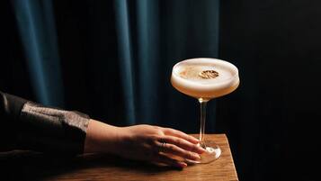 A hand holding a martini glass on a wooden table.