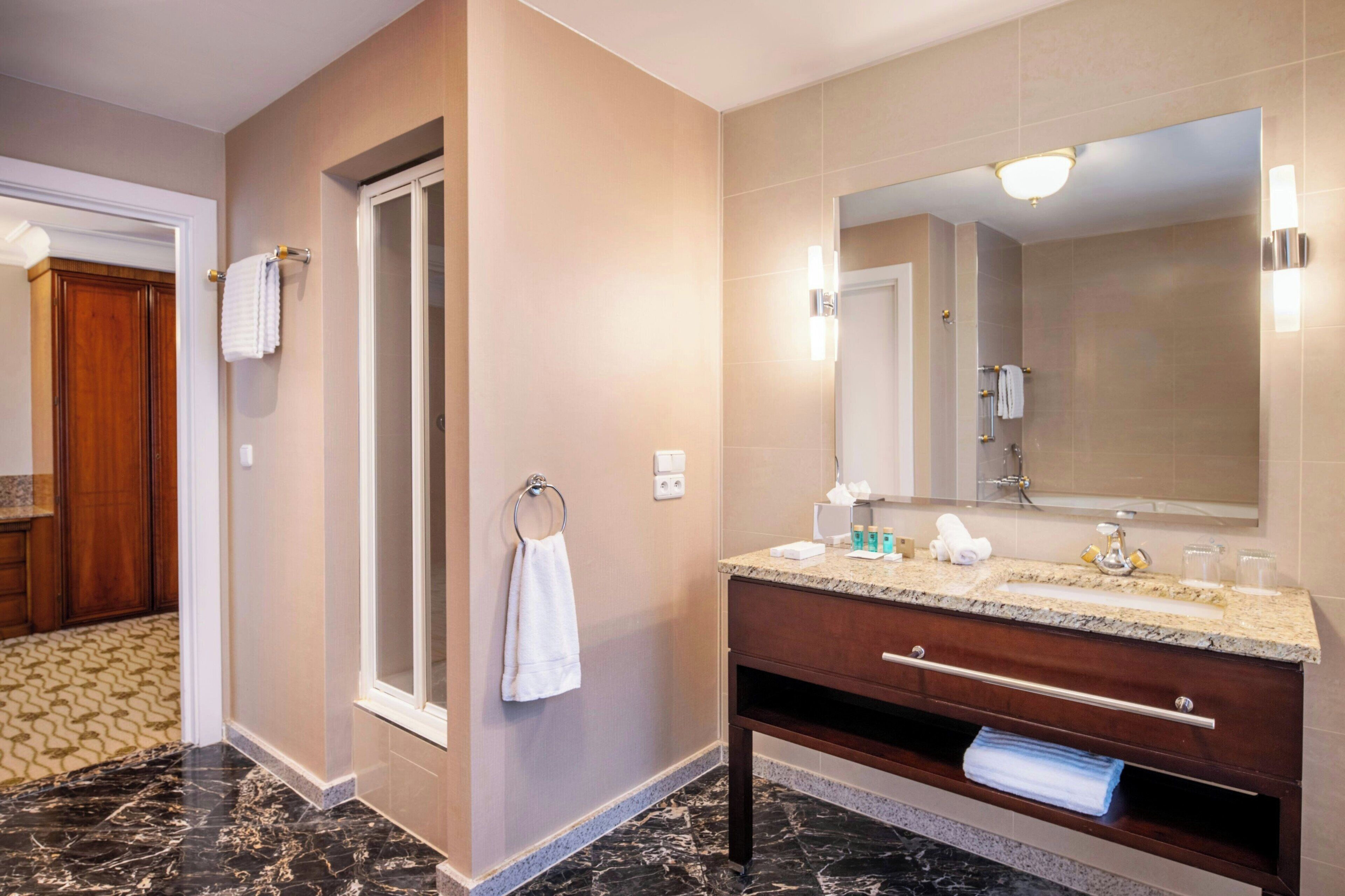 Une salle de bain moderne avec un sol en marbre, un grand miroir et un meuble-lavabo en bois.