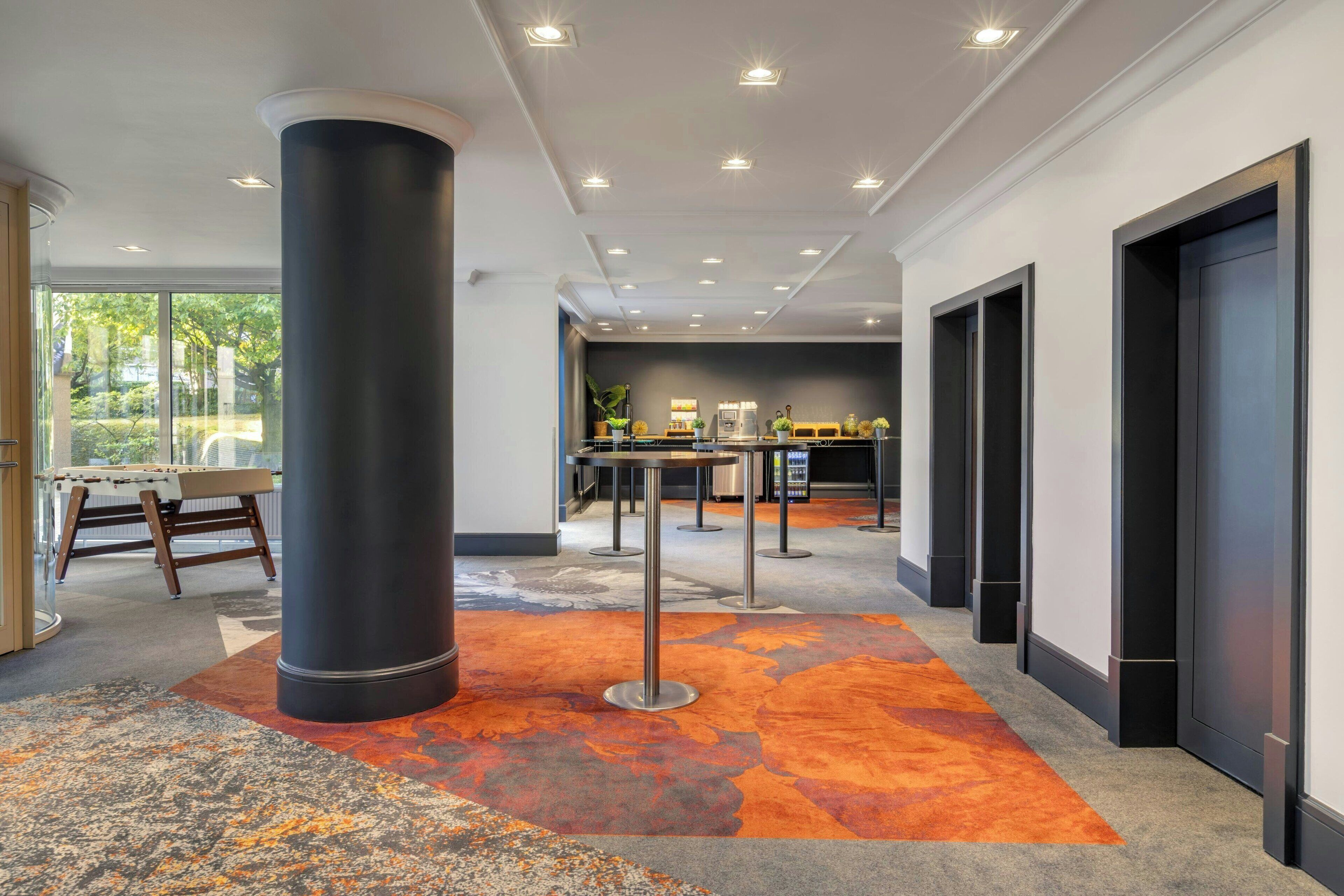 A modern lobby with a central column, a pool table, a bar area, and a carpeted floor.