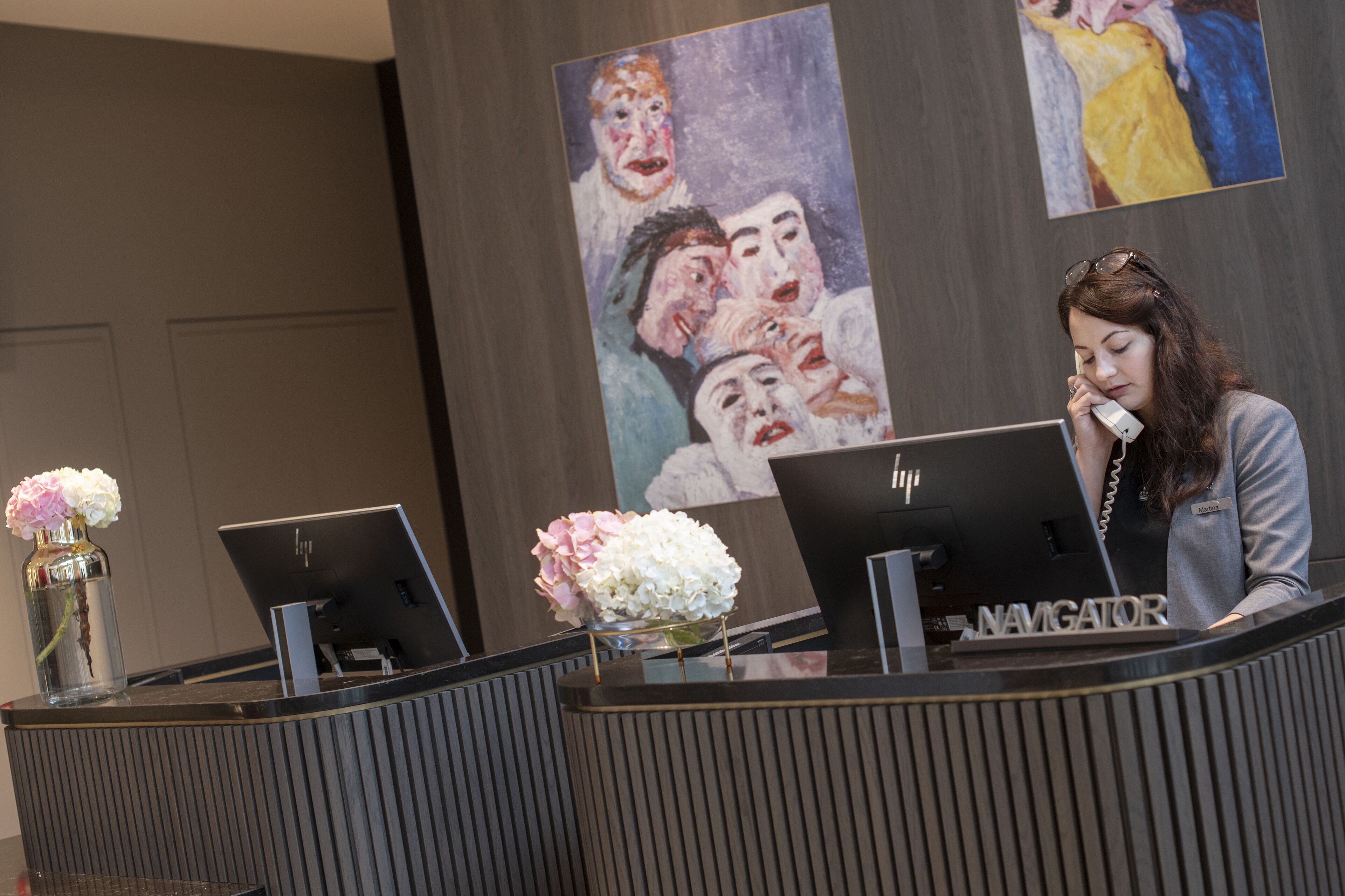 Un comptoir d’accueil avec deux ordinateurs HP, un vase de fleurs et un tableau accroché au mur.