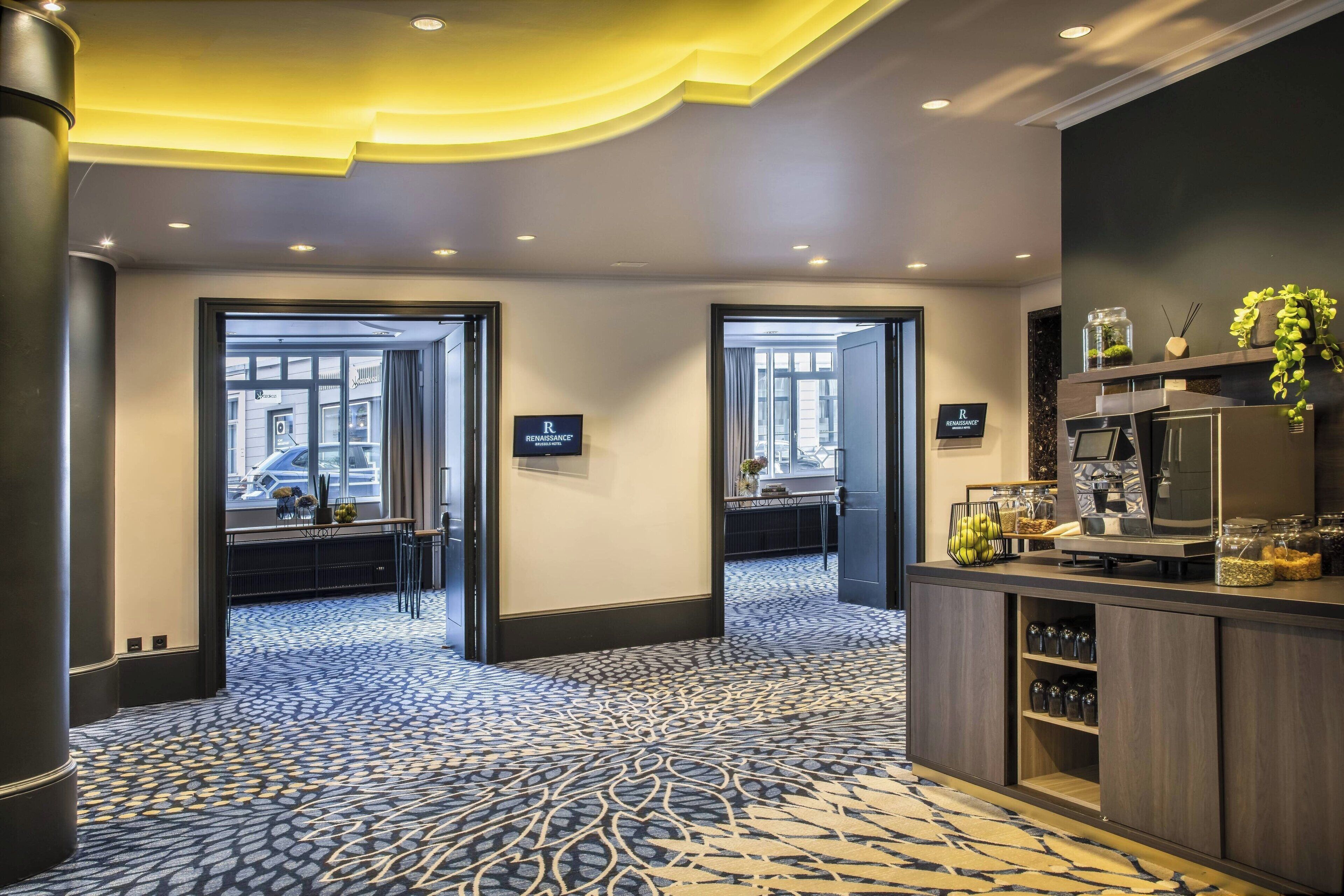 A hotel lobby with a patterned carpet, a reception desk with amenities, and two doors leading to other areas.