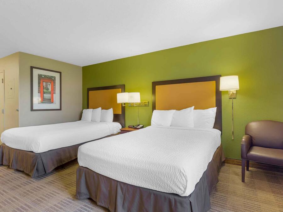 A hotel room with two beds, a chair, and a framed picture on the wall.