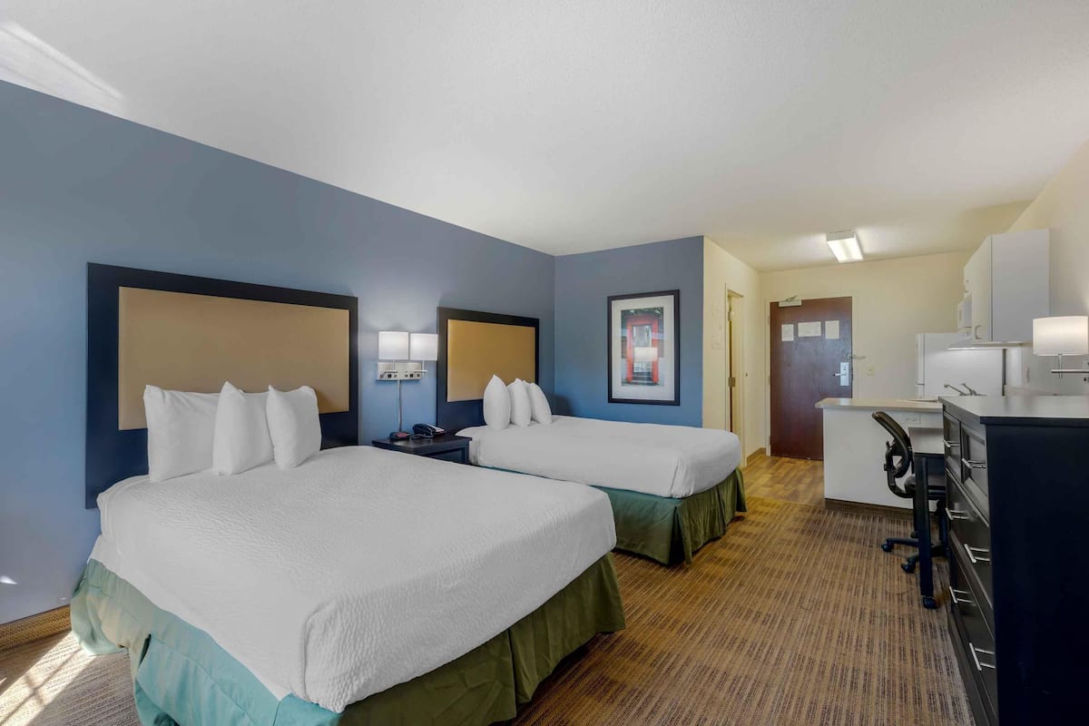 A hotel room with two beds, a desk, and a kitchenette.