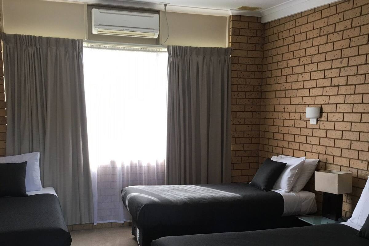 A hotel room with two beds, a desk, a chair, and a window with curtains.