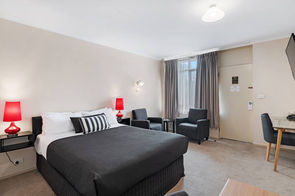 A hotel room with a large bed, two bedside tables with lamps, a desk, and a chair.