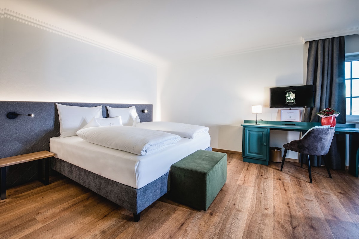 Habitación de hotel ordenada con cama, escritorio, silla y televisor.