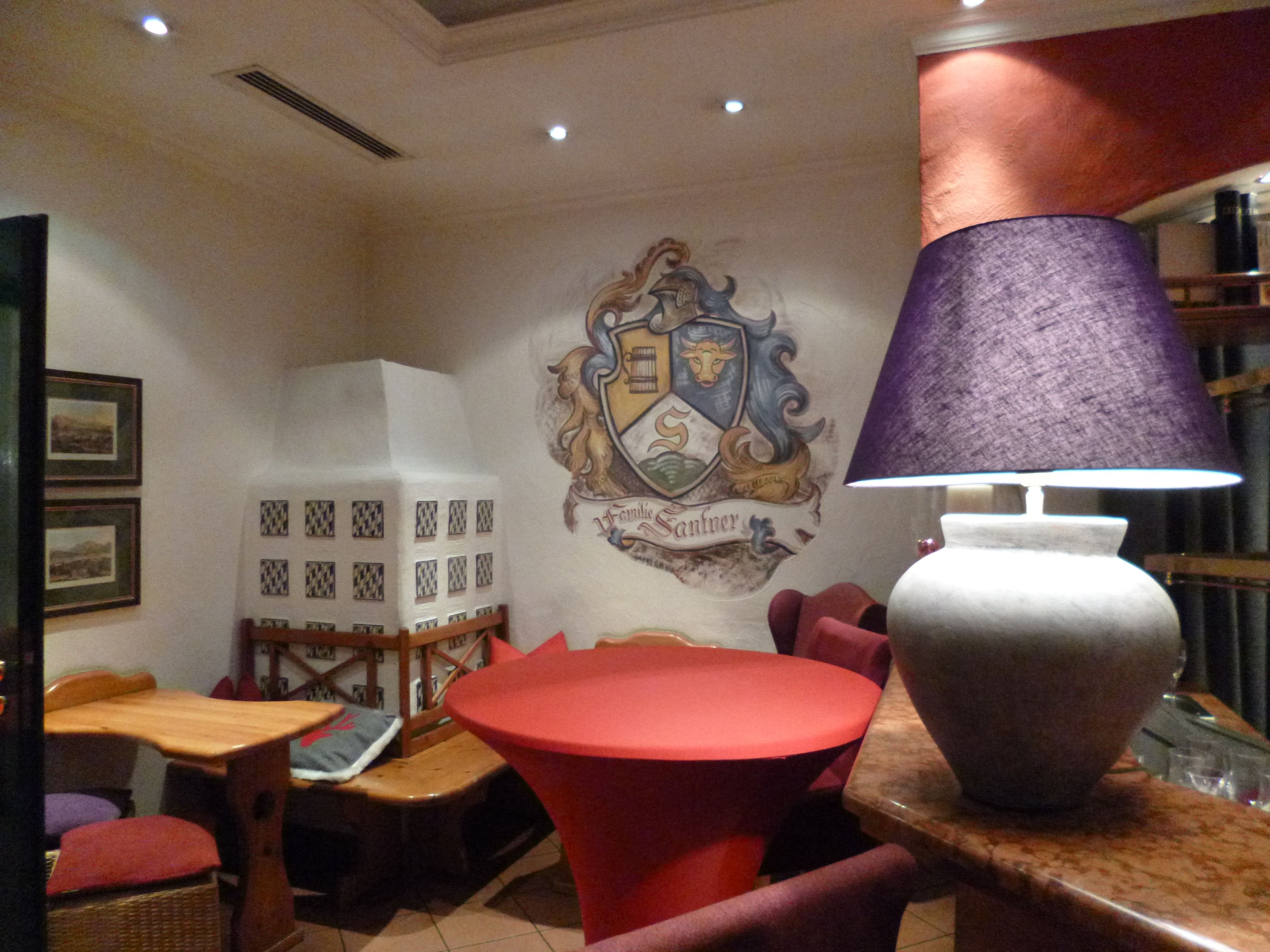 A room with a round red table, a purple lamp, and a shield-shaped wall decoration.
