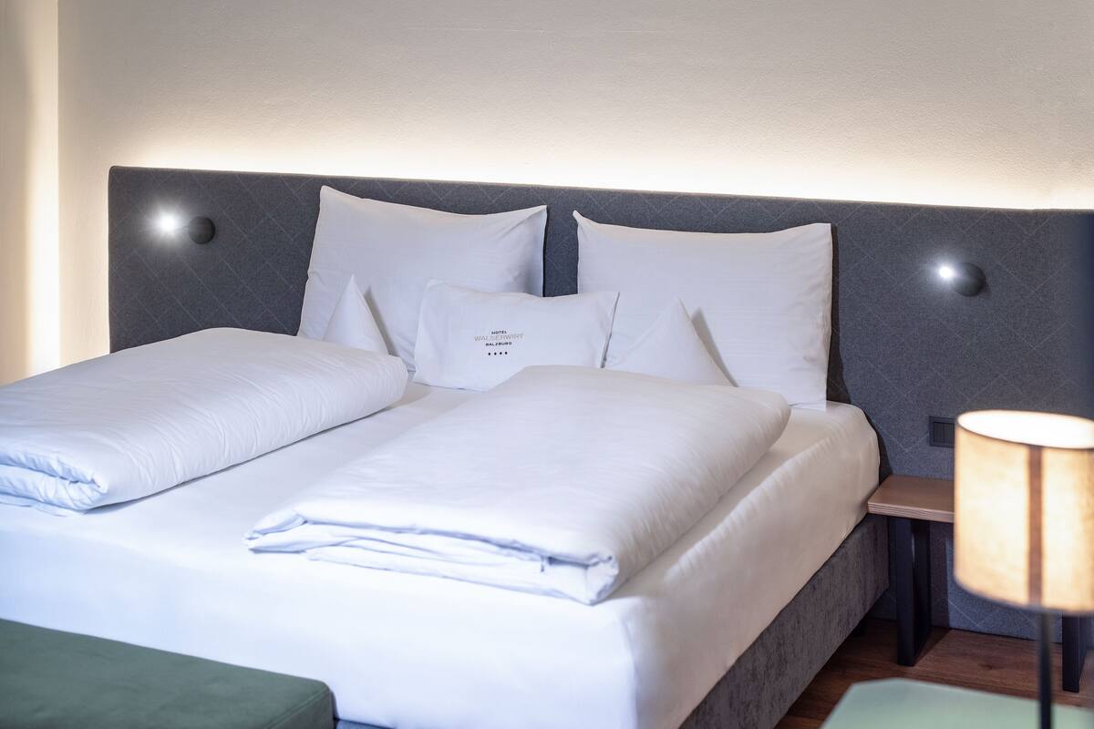 Una cama doble con ropa de cama blanca y un cabecero con lámparas circulares.
