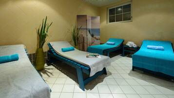 Two beds with blue bedding and a central bed with white bedding, complemented by a potted plant and a framed beach scene.