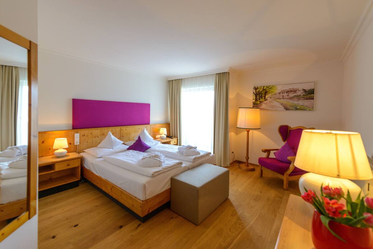 Habitación de hotel con cama, una silla, mesita de noche, lámpara y un cuadro en la pared.