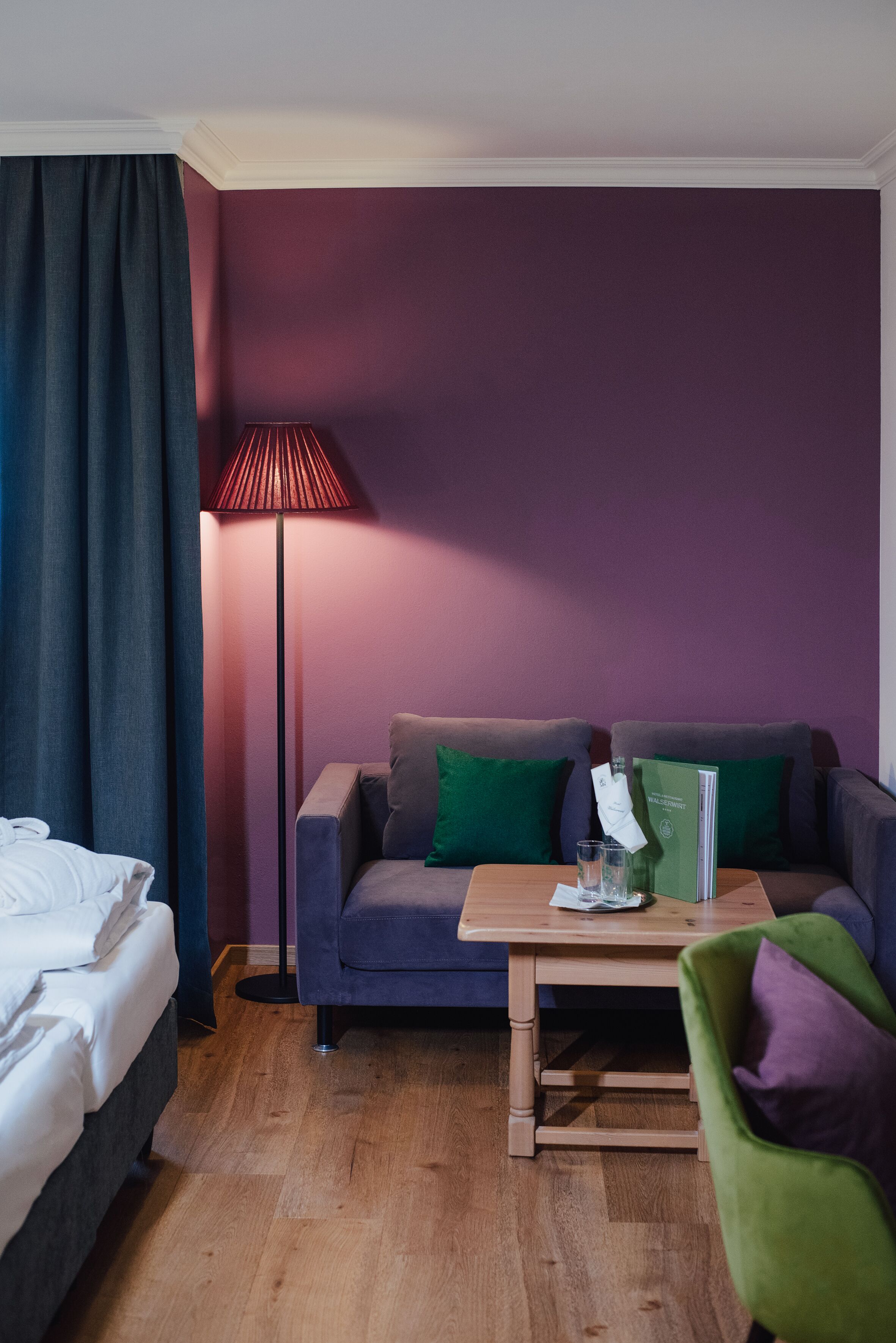 Habitación de hotel con cama, sofá, una mesita, una lámpara de pie y una silla verde.