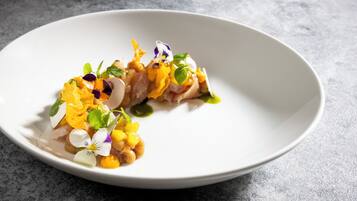 Une assiette blanche contenant un plat composé de poisson et de légumes, posée sur une surface grise texturée.