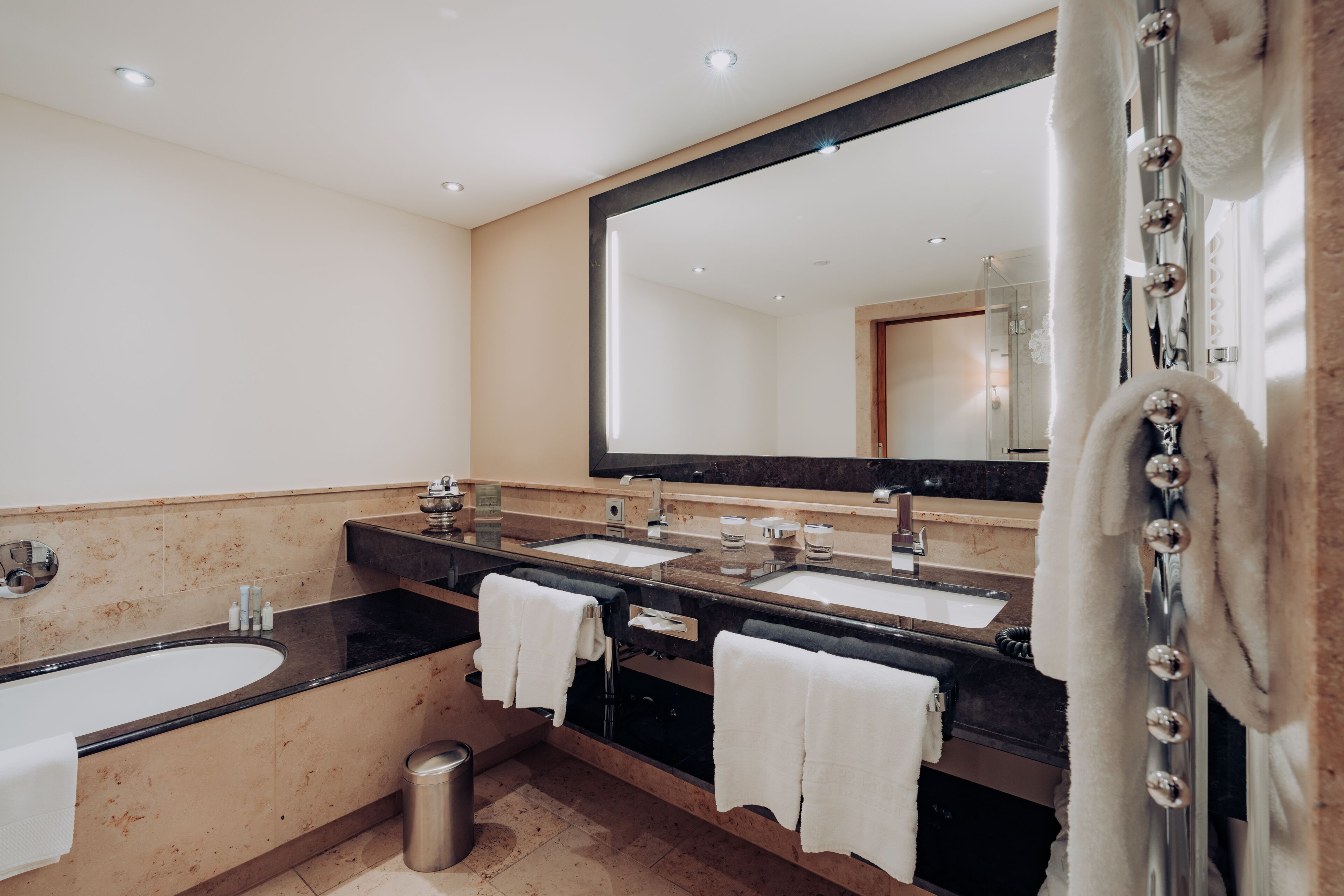 A modern bathroom with a large mirror, two sinks, a bathtub, and a shower.