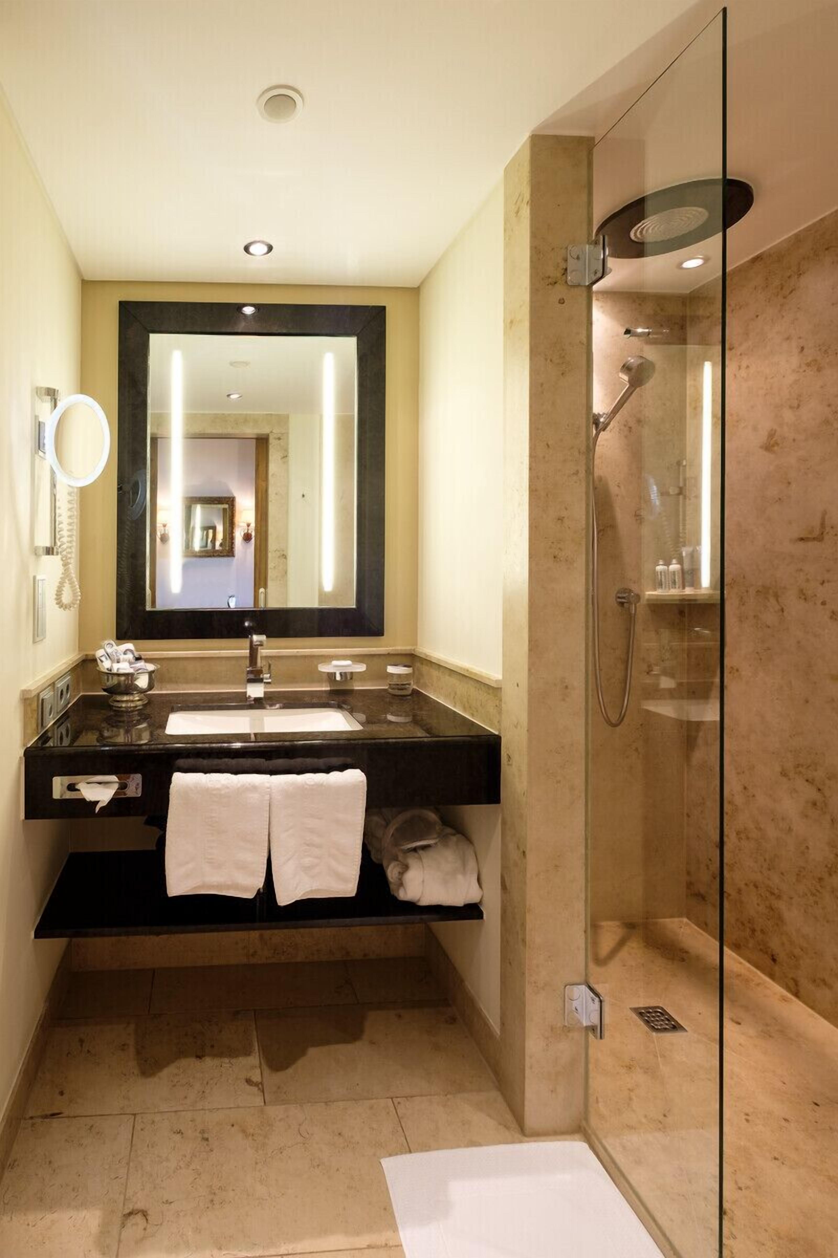 Un baño moderno con un espejo grande, un lavamanos y una ducha con mampara de vidrio.