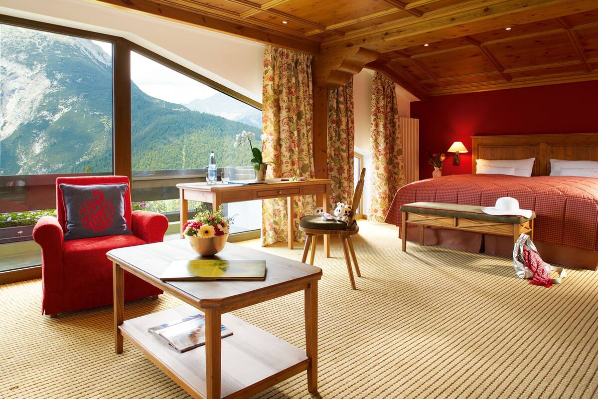 Una habitación con cama, escritorio, silla y mesa. Se ve una ventana con vista a la montaña.