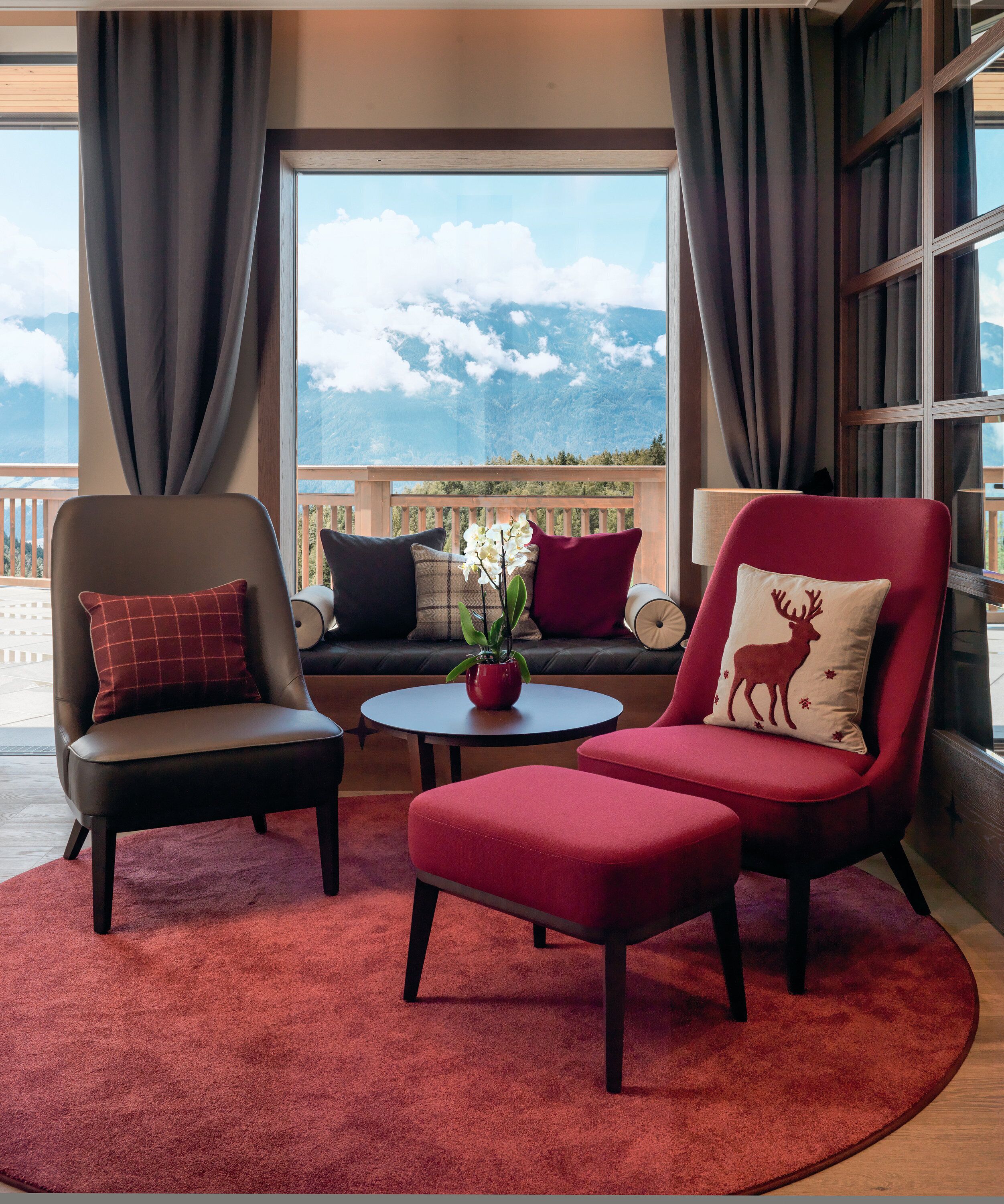A room with a view of mountains, a red sofa, a red armchair, and a small table with a plant.
