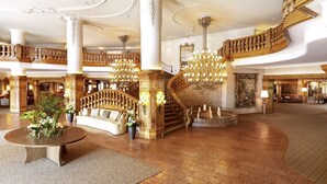 Um amplo hall de entrada com escadaria central, lustres elaborados e um espaço de estar com uma mesa de centro.