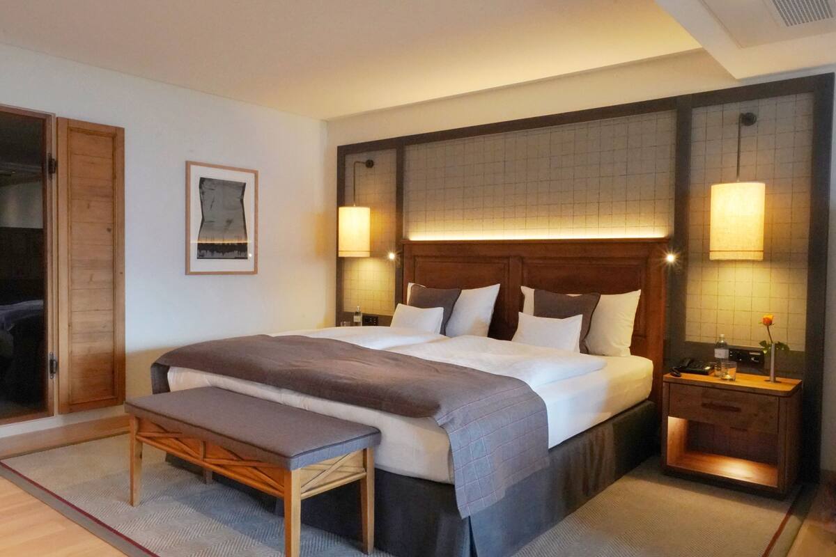 Una habitación de hotel con una cama grande, mesitas de noche, un banco y un espejo.