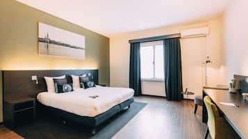 A modern hotel room with a large bed, a desk, and a cityscape view.