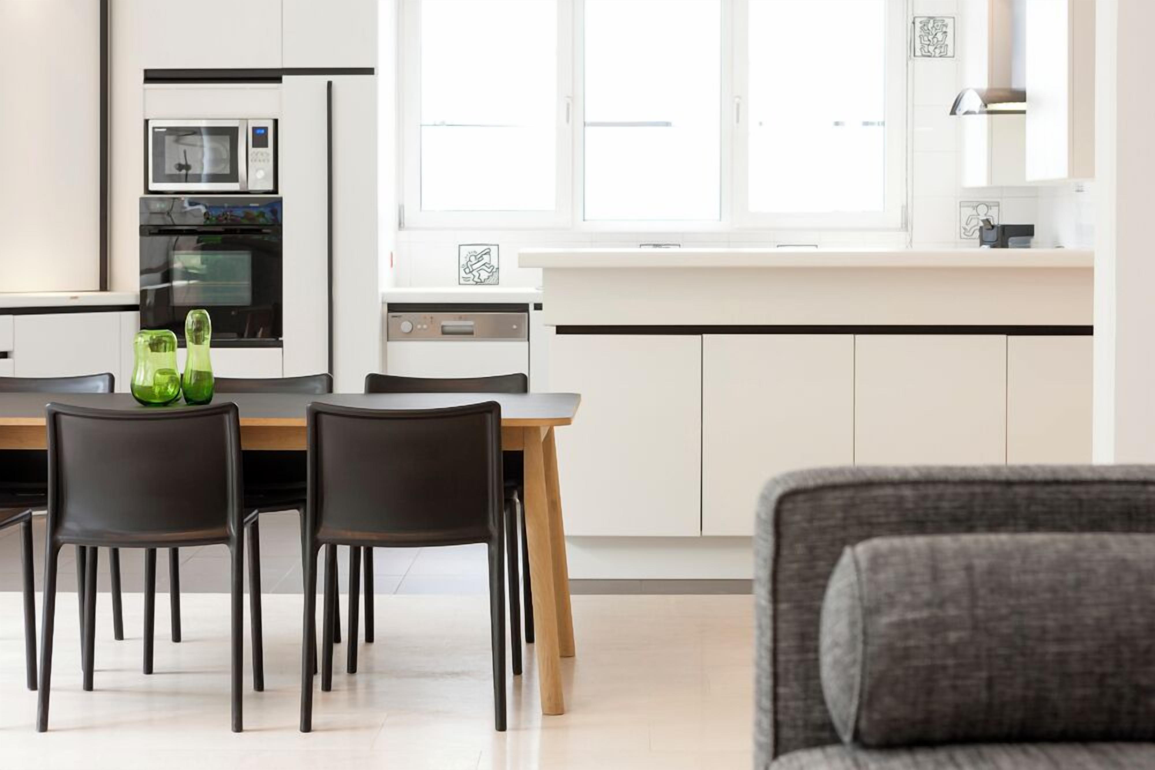 A modern kitchen with a dining table, chairs, and a gray sofa.