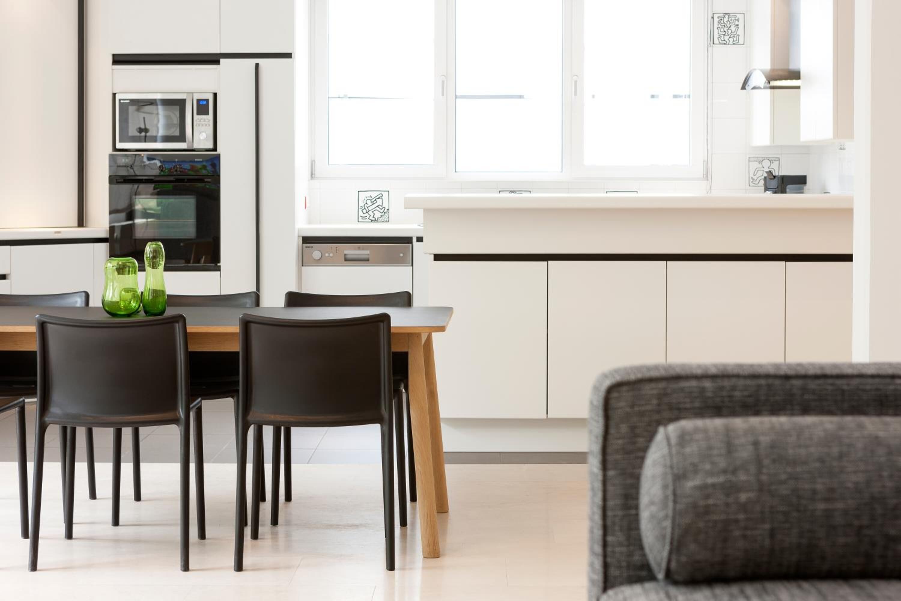 A modern kitchen with white cabinets, a wooden dining table, and black chairs.