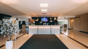 A modern hotel lobby with a reception desk, a large screen TV, pendant lighting, and a potted plant. - Hotel Ter Elst (Edegem)