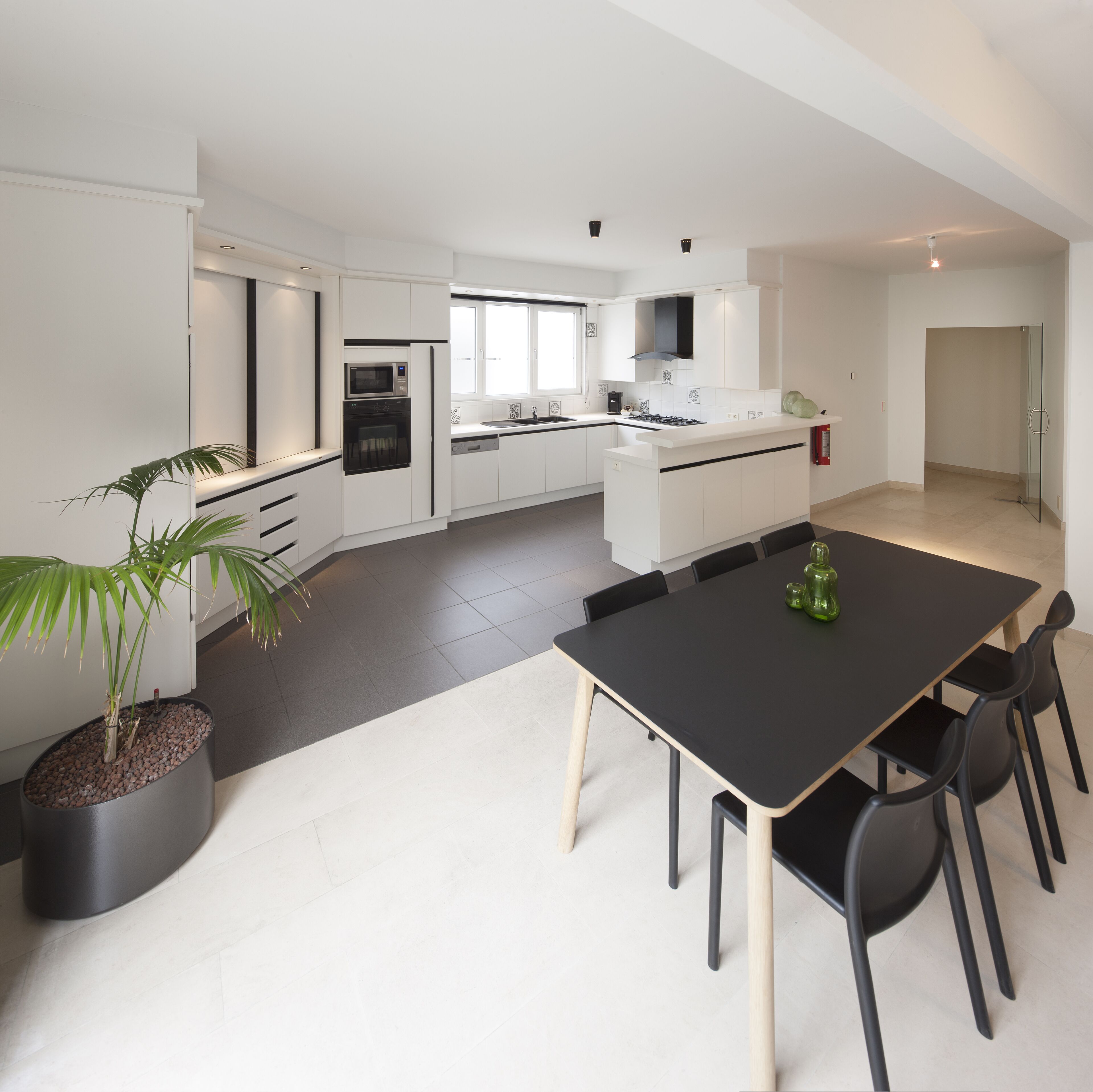 A modern kitchen with white cabinetry, a black dining table, and a potted plant.