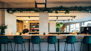 A bar area with a wooden counter, green bar stools, and a person working behind the bar. - Hotel Ter Elst (Edegem)