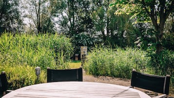 Mesa redonda de madera con dos sillas en un jardín, rodeado de follaje exuberante y árboles.