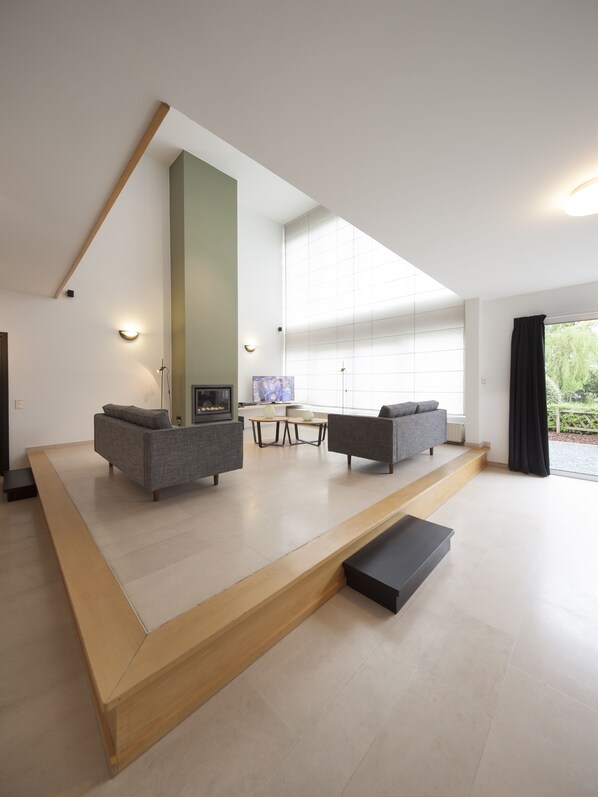 Una sala de estar moderna con un espejo grande, dos sofás grises, una mesa de centro y un televisor.