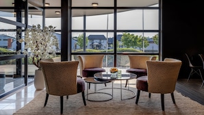 A modern interior with large windows, wicker chairs, a round table, and a potted plant. - Hotel Ter Elst (Edegem)