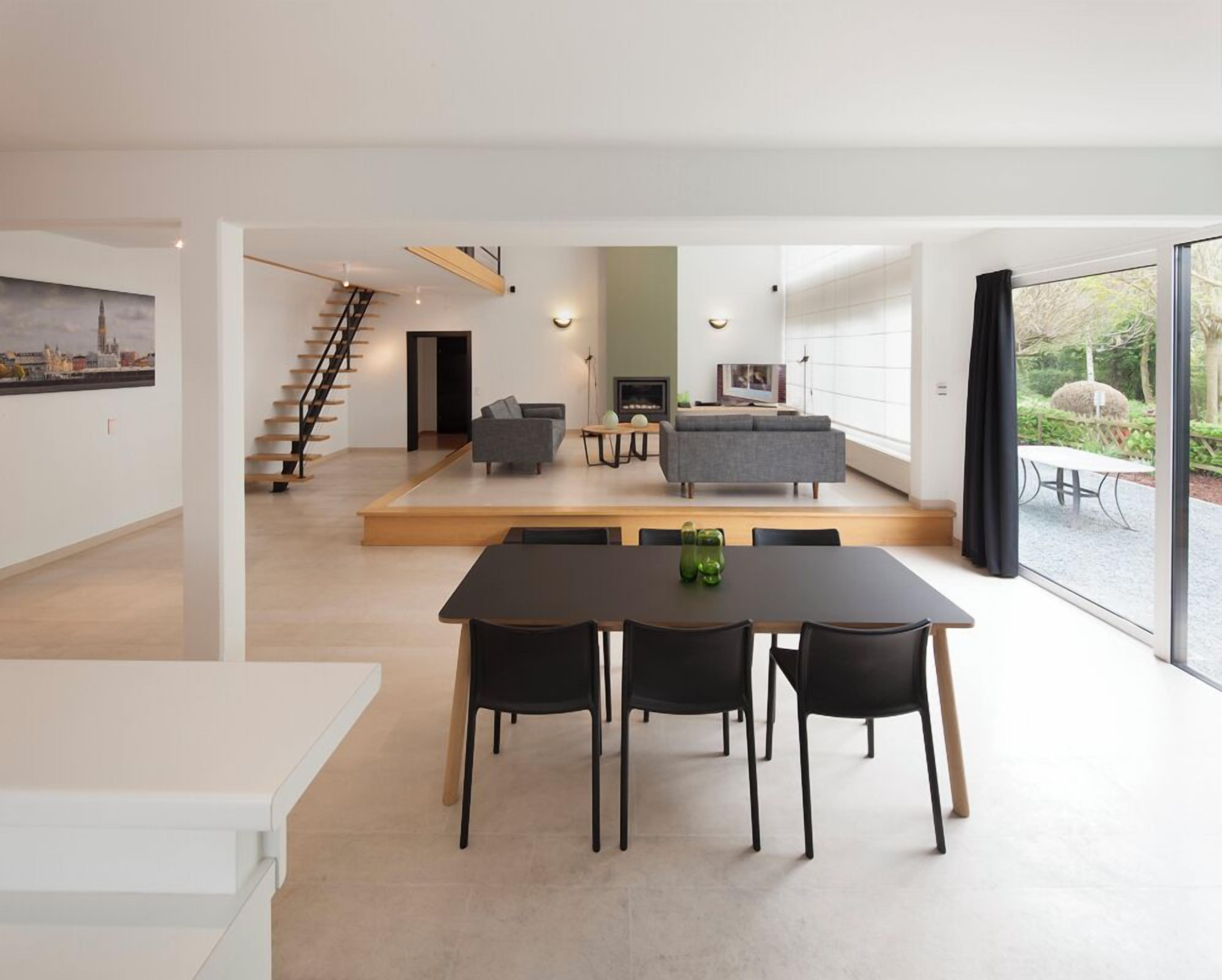 Un intérieur moderne comprenant un coin repas, des canapés, un escalier et une grande fenêtre.